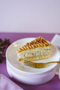 fatia de bolo de massa branca com camada de recheio de doce de leite e creme de noz servido num prato com garfo